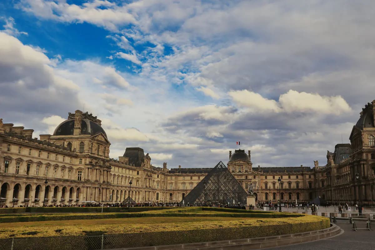 The glass pyramid in the courtyard of the Louvre in Paris, between the palace wings under a cloudy sky