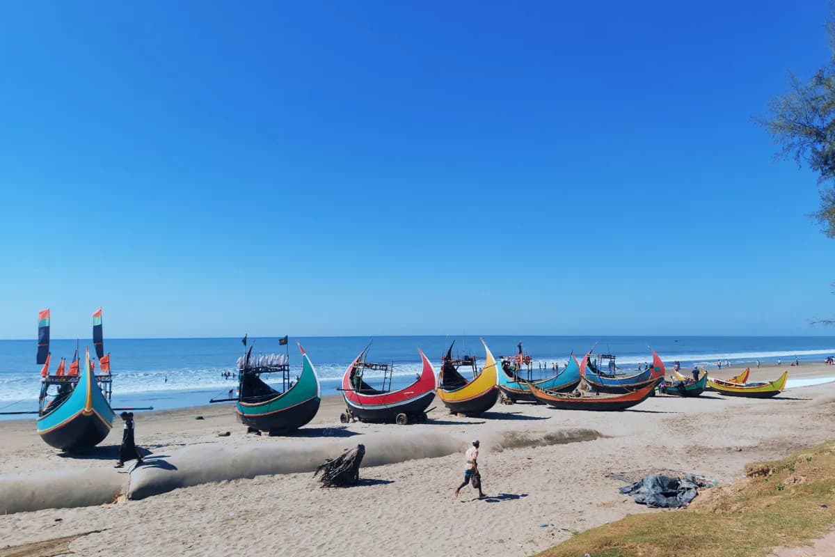 Brightly painted wooden fishing boats with curved hulls resting on the sand beside the sea under a clear sky