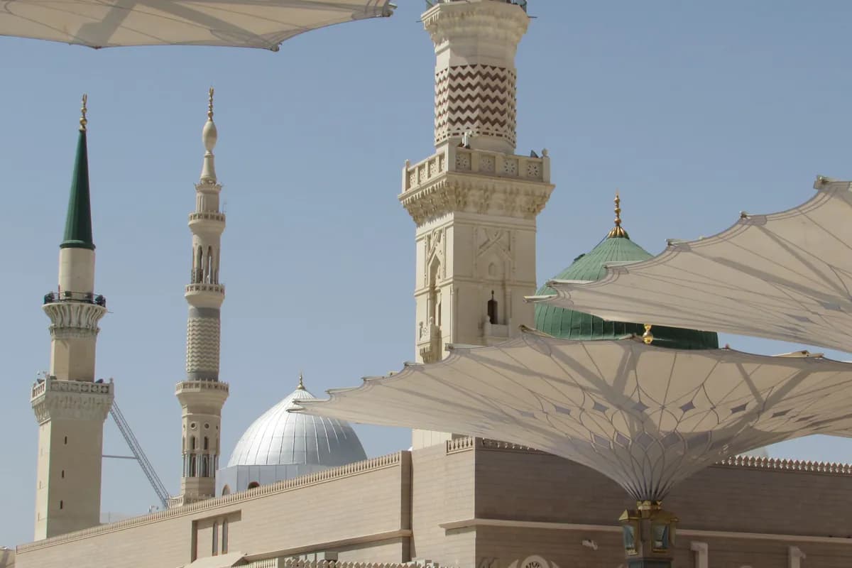 Minarets, a silver dome and the green dome of the Prophet's Mosque behind open shade canopies
