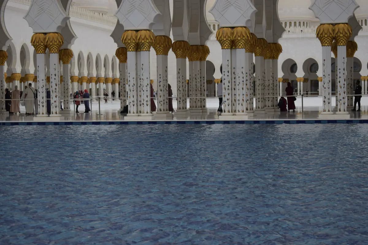 White columns with floral inlay and gold capitals beside a blue pool in the courtyard of the Sheikh Zayed Grand Mosque