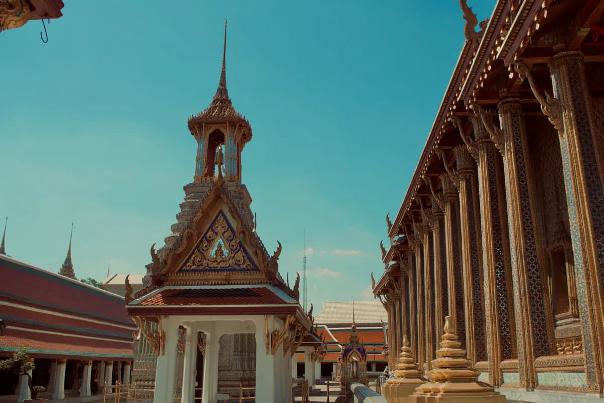A bell tower with a gilded gable and a row of gilded, mosaic covered columns at Wat Phra Kaew in Bangkok