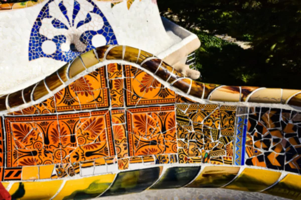 Close view of broken tile mosaic in orange, yellow, blue and white on a curving bench in Park Güell