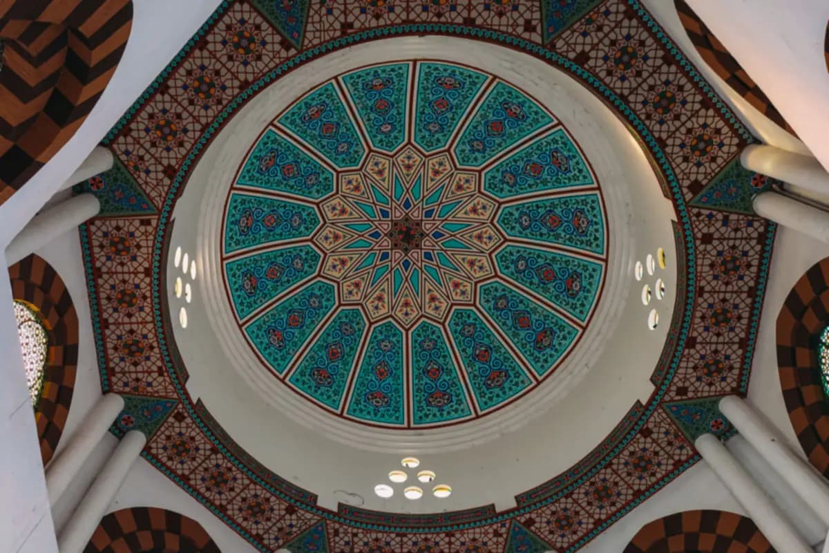 Looking up into a dome painted with turquoise, blue and red geometric and floral patterns, ringed by small windows