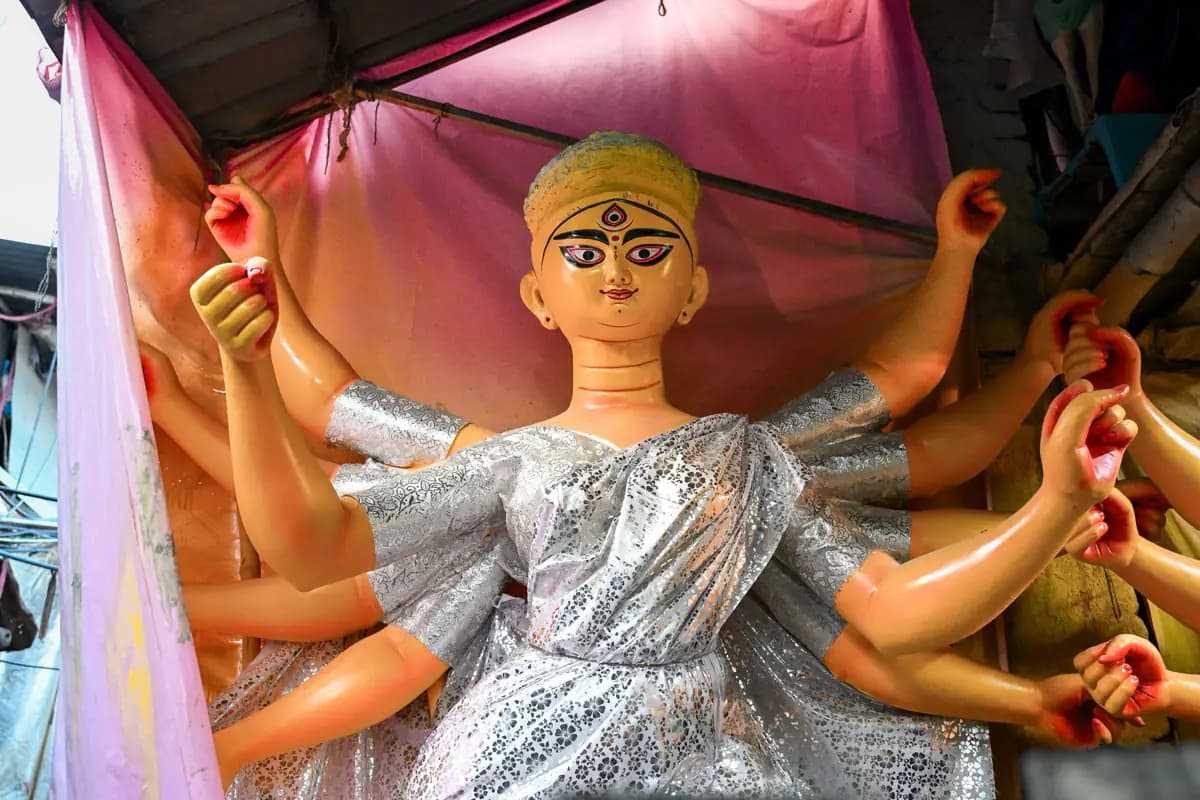 A clay idol of the goddess Durga with many arms, draped in silver cloth under a pink canopy in Kumartuli, Kolkata