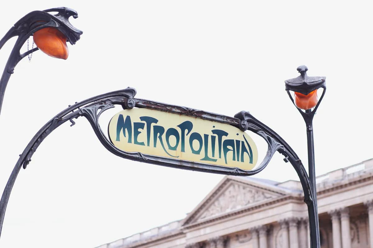 An Art Nouveau Métro sign reading Metropolitain on curved iron posts with orange lamps, in front of a stone building