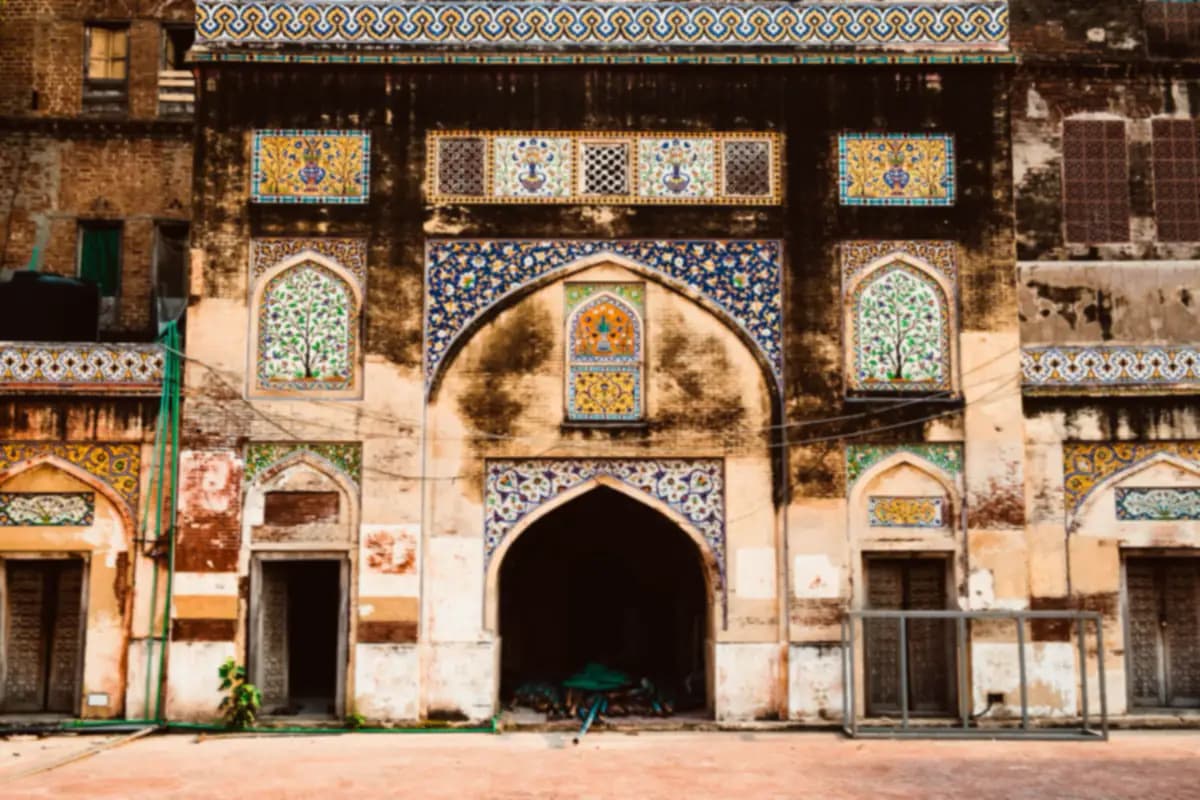 Painted tile panels with flowers and vases around an arched doorway on an old brick building in Lahore