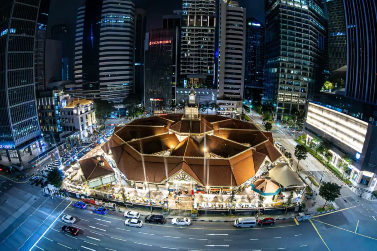 Aerial view at night of the octagonal Lau Pa Sat market hall and clock tower, with outdoor tables and office towers around it
