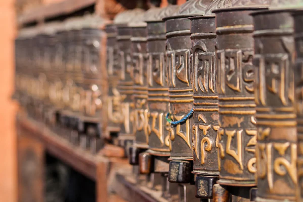 A row of metal prayer wheels embossed with Tibetan script at Swayambhunath in Kathmandu