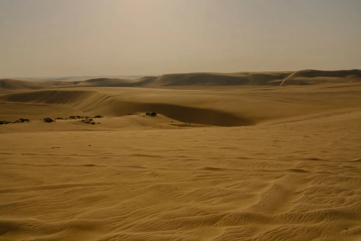 Rippled sand and rolling dunes under a hazy sky in the desert near Doha
