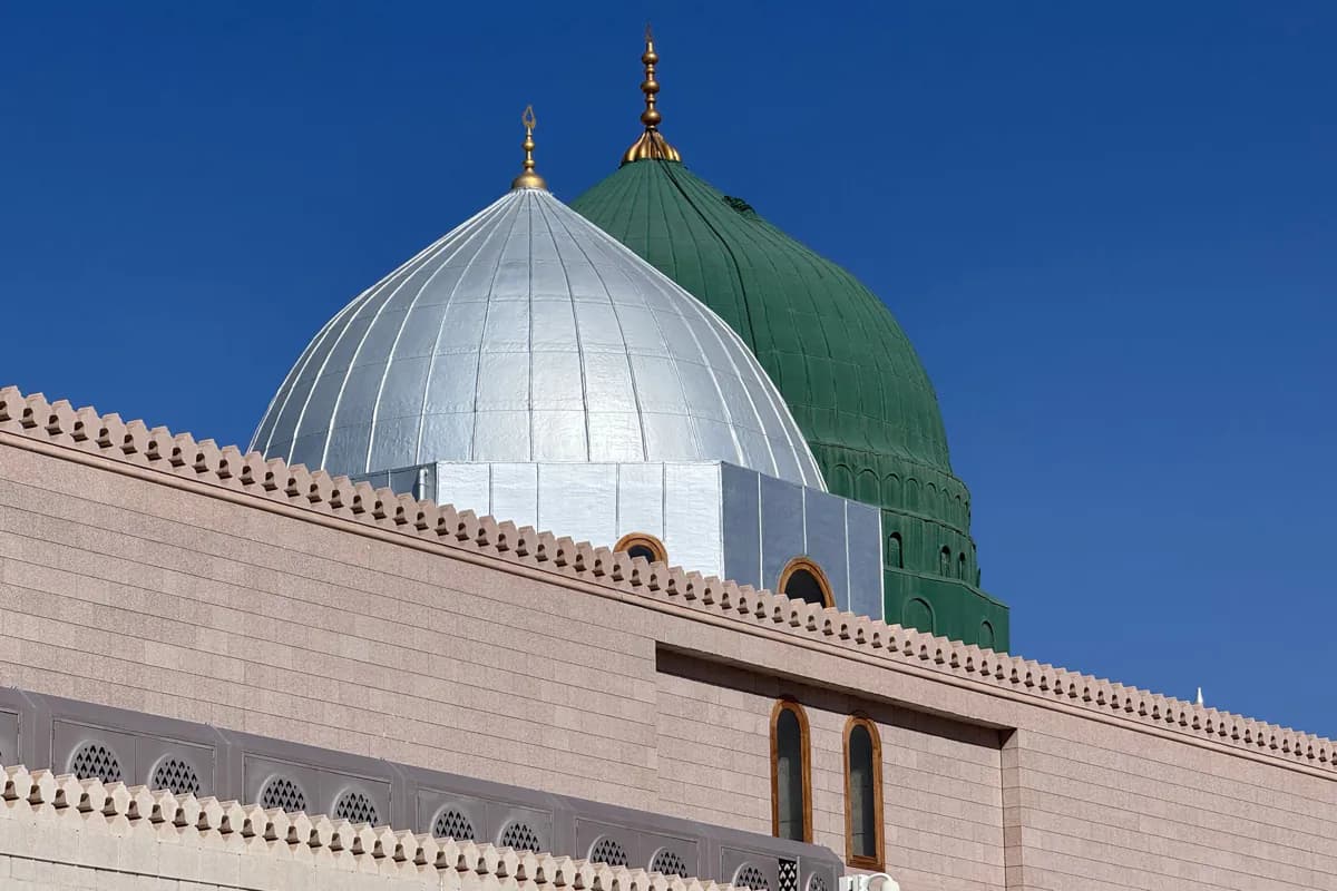 The silver dome and the green dome of the Prophet's Mosque against a deep blue sky