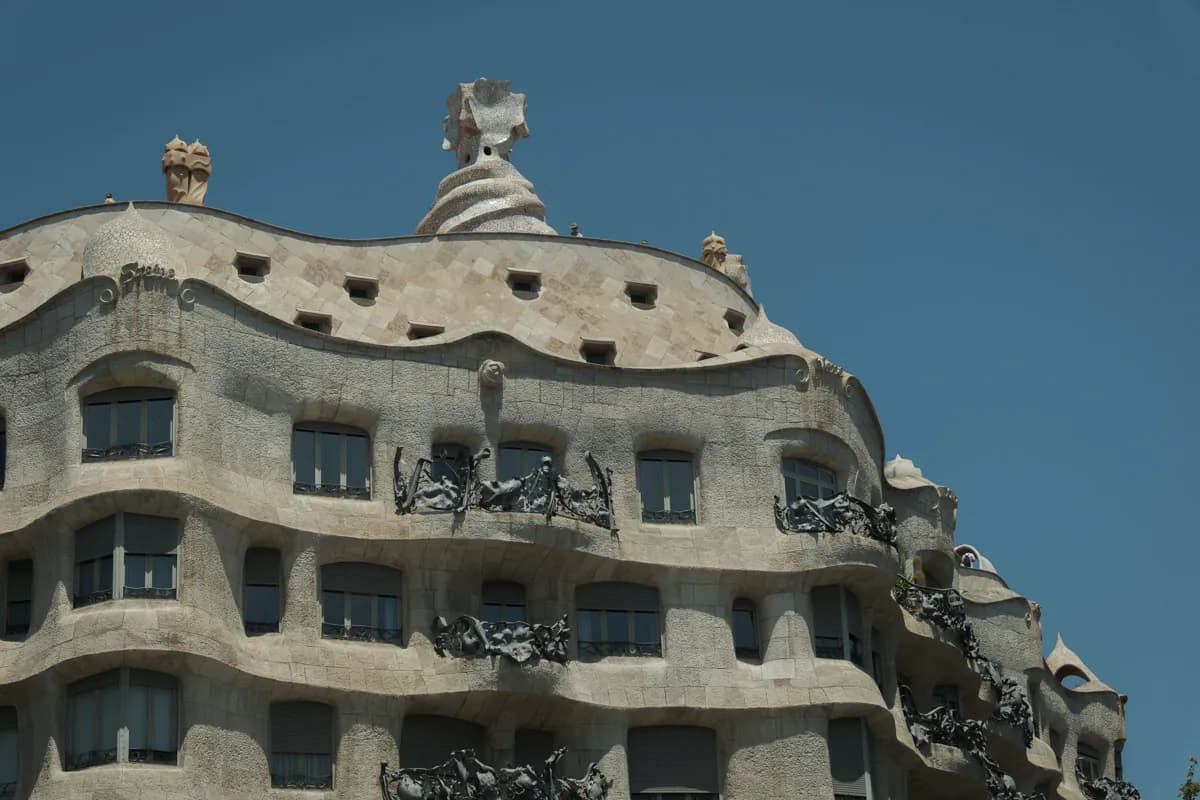 The wavy stone facade, iron balconies and rooftop chimneys of Casa Milà in Barcelona against a clear blue sky