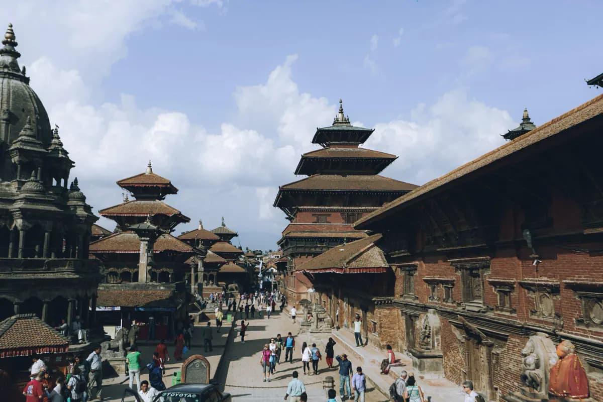 Tiered pagoda roofs and a carved stone temple around Patan Durbar Square, with visitors walking across the paved square